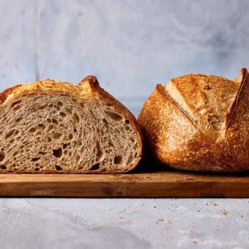 Anschnitt eines lockeren Weizensauerteigbrotes auf einem Holzbrett, das die grobe Porung der Krume und die knusprige Kruste zeigt – gebacken ohne Knetmaschine nach einem einfachen Anfänger-Rezept.
