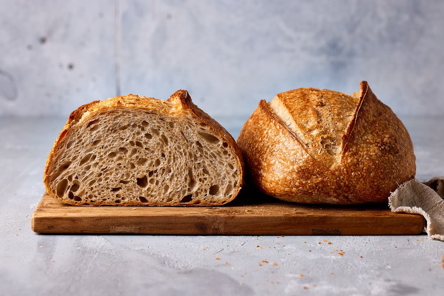 Anschnitt eines lockeren Weizensauerteigbrotes auf einem Holzbrett, das die grobe Porung der Krume und die knusprige Kruste zeigt – gebacken ohne Knetmaschine nach einem einfachen Anfänger-Rezept.