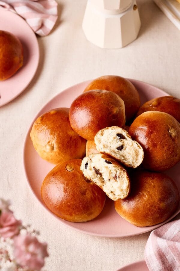 Goldbraune Rosinenbrötchen wie vom Bäcker auf einem rosa Teller, aufgebrochen mit saftiger Krume und prallen Rosinen.