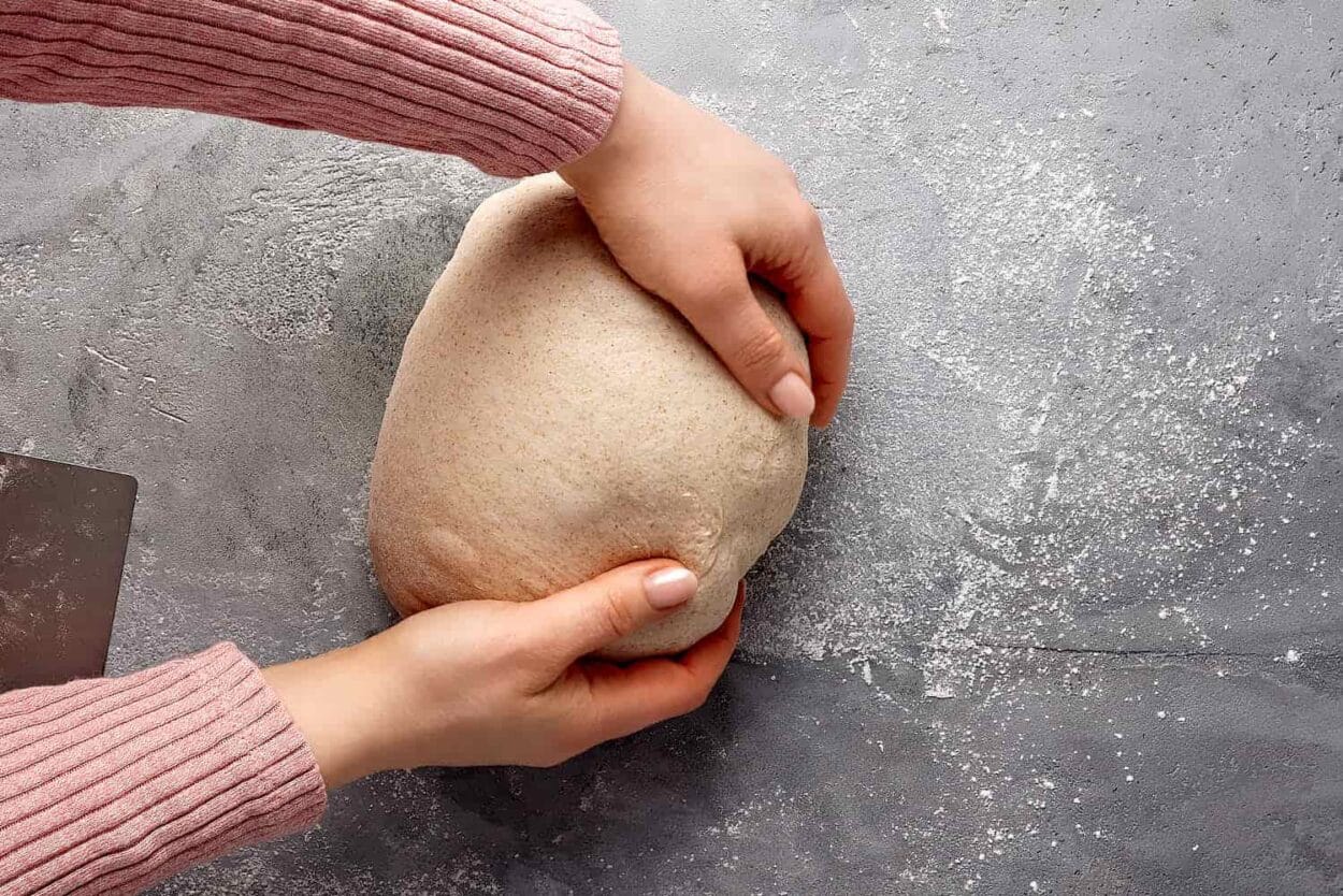 Sauerteigbrot mit Spannung formen auf der leicht bemehlten Arbeitsfläche. 