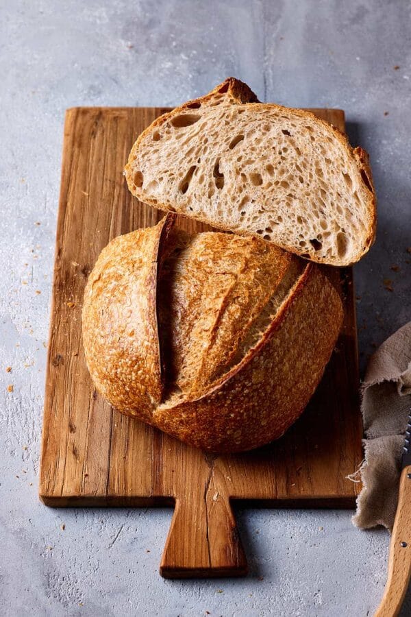 Einfaches Weizensauerteigbrot aufgeschnitten auf einem Holzbrett mit lockerer Krume und goldbrauner Kruste.